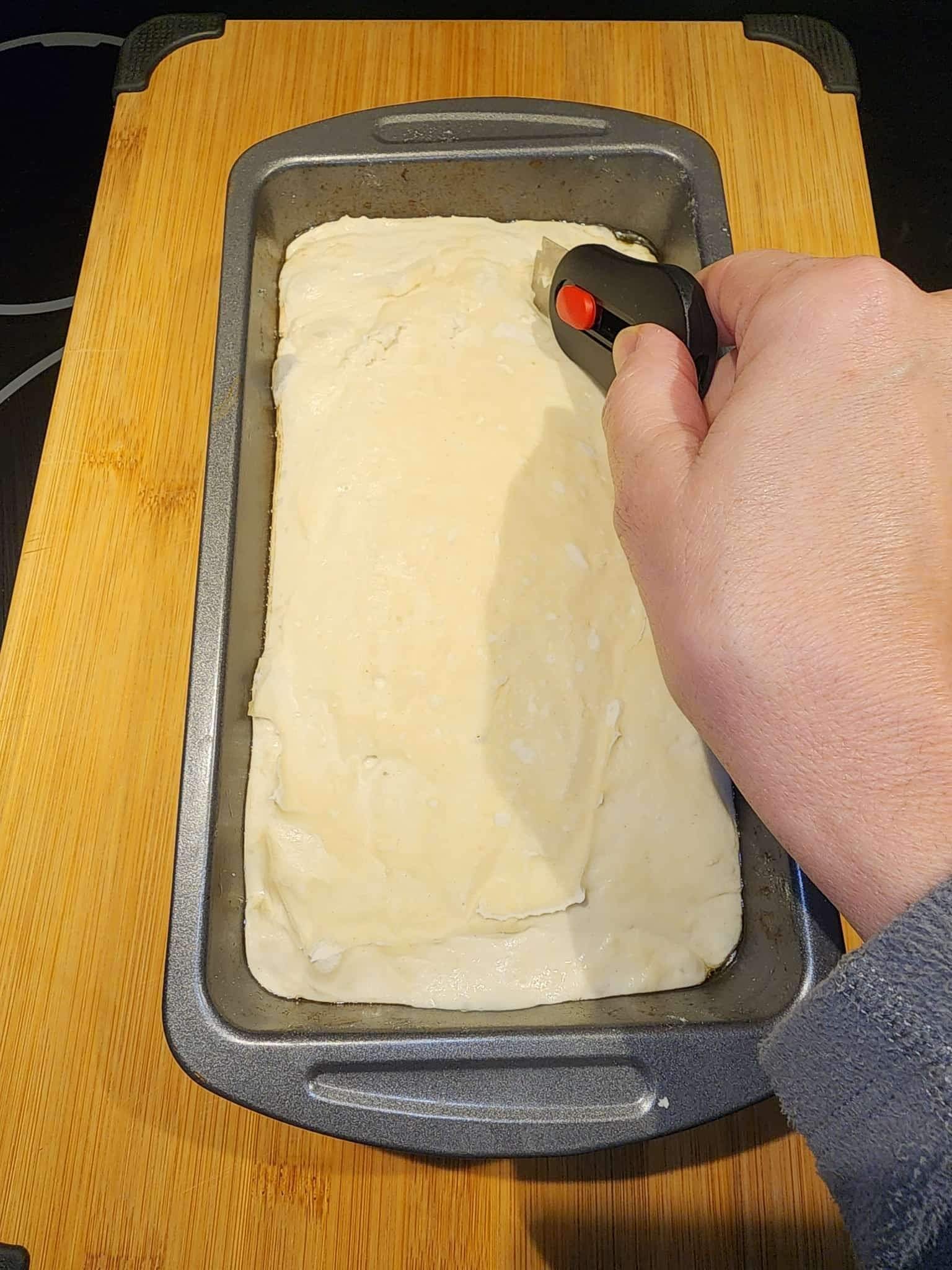 Sourdough in a bread pan being scored by a blade tool.