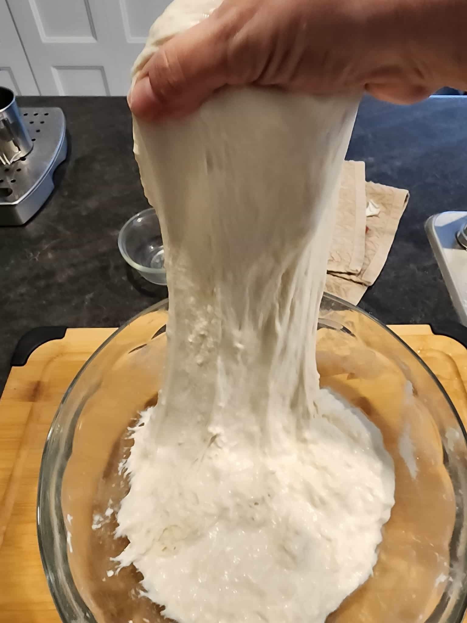 Hand stretching sourdough in a glass bowl.